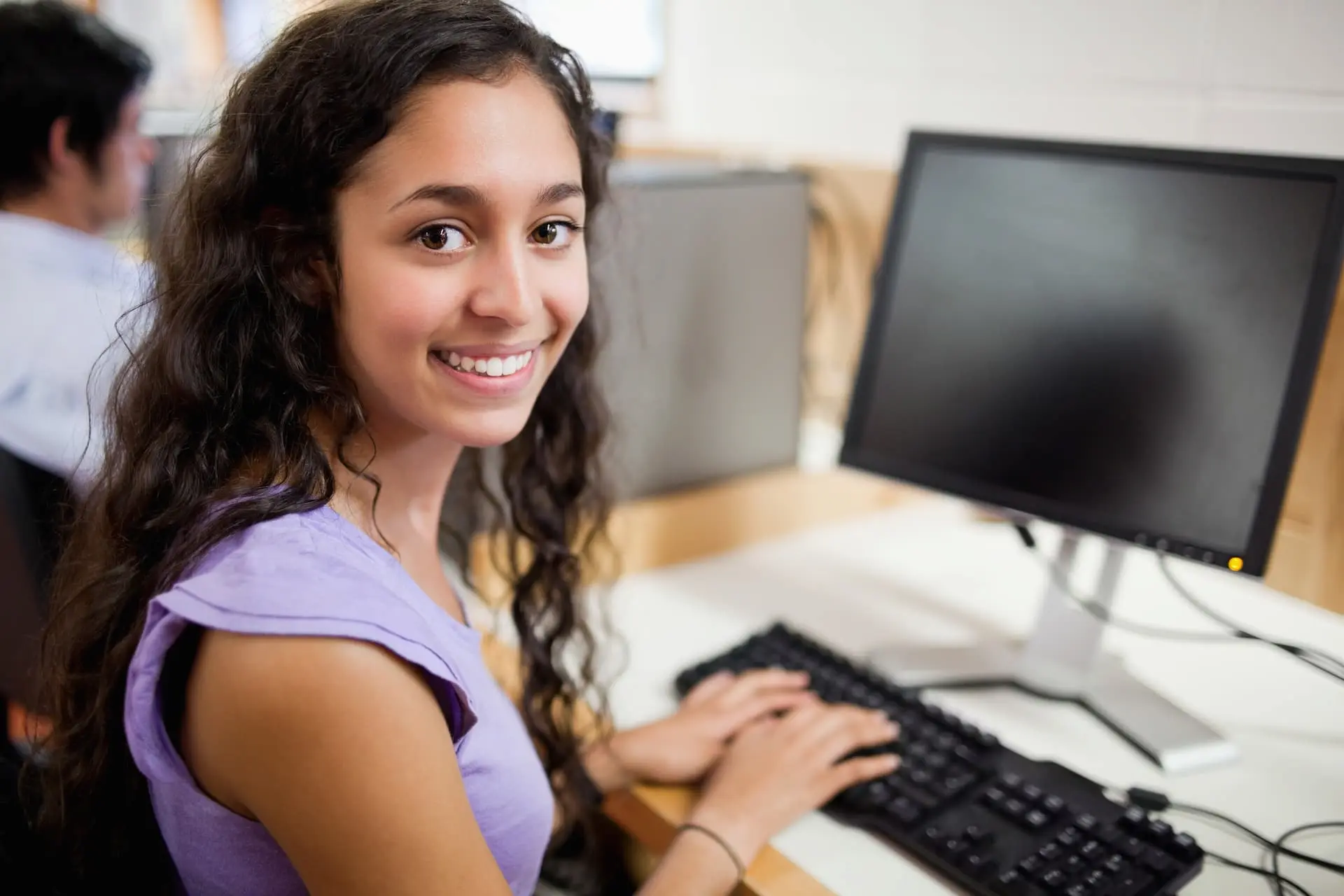 A student looking to the side and smiling while at a computer.