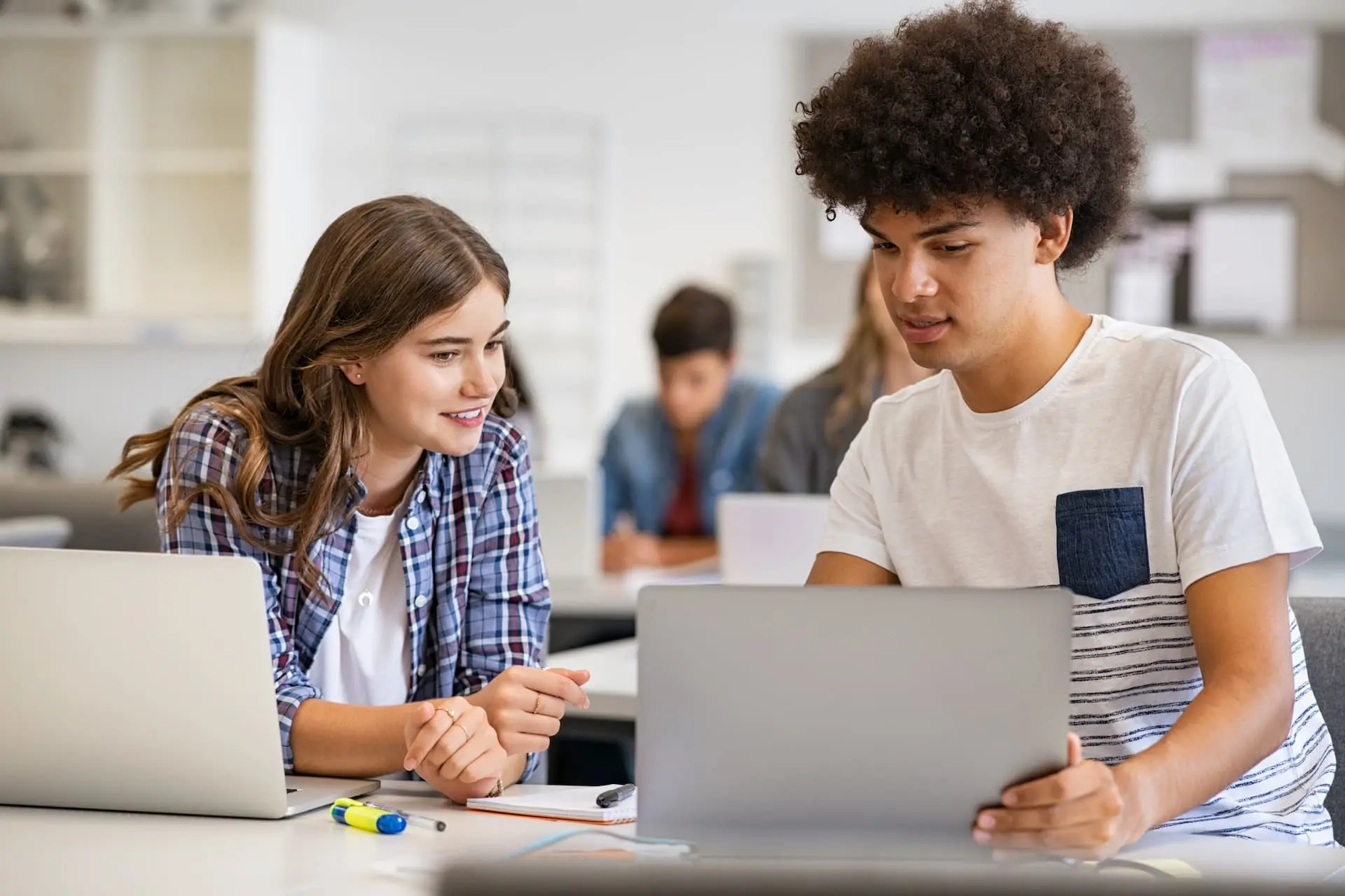 Two students working together, looking at a laptop screen.