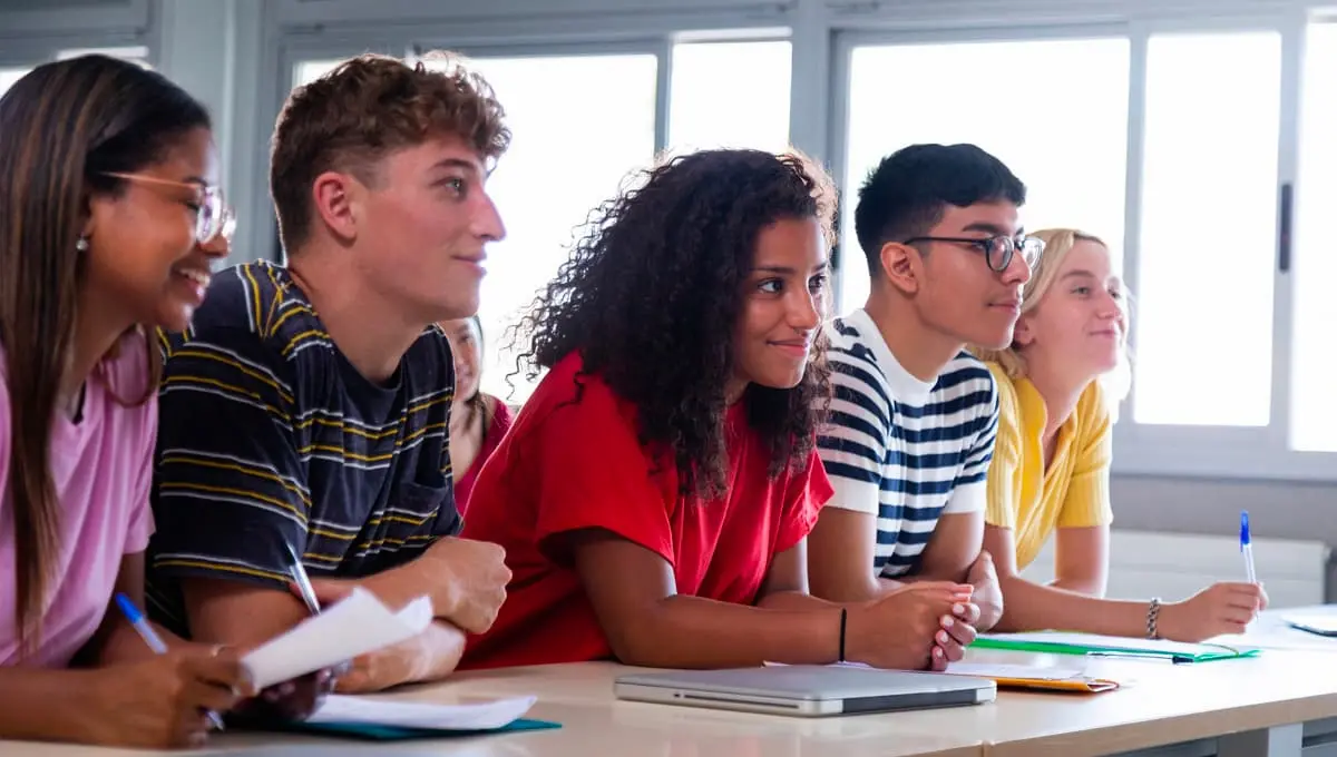 A group of students sitting beside eachother at their desks and smiling.