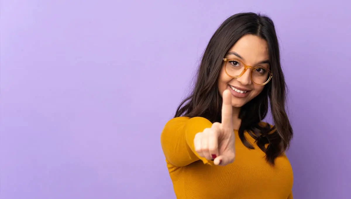 A young woman smiling making the number one with her finger.