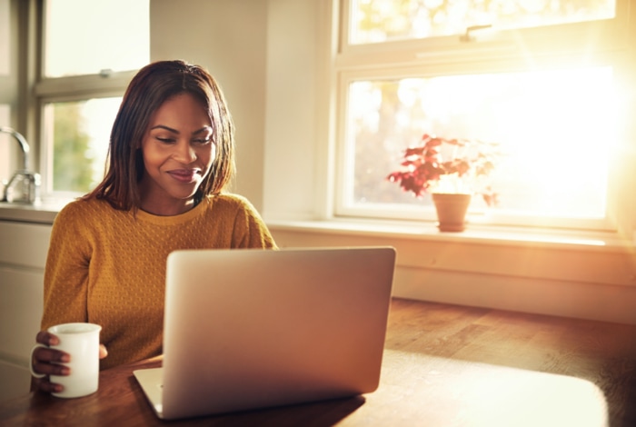 Woman having a drink and using the laptop.