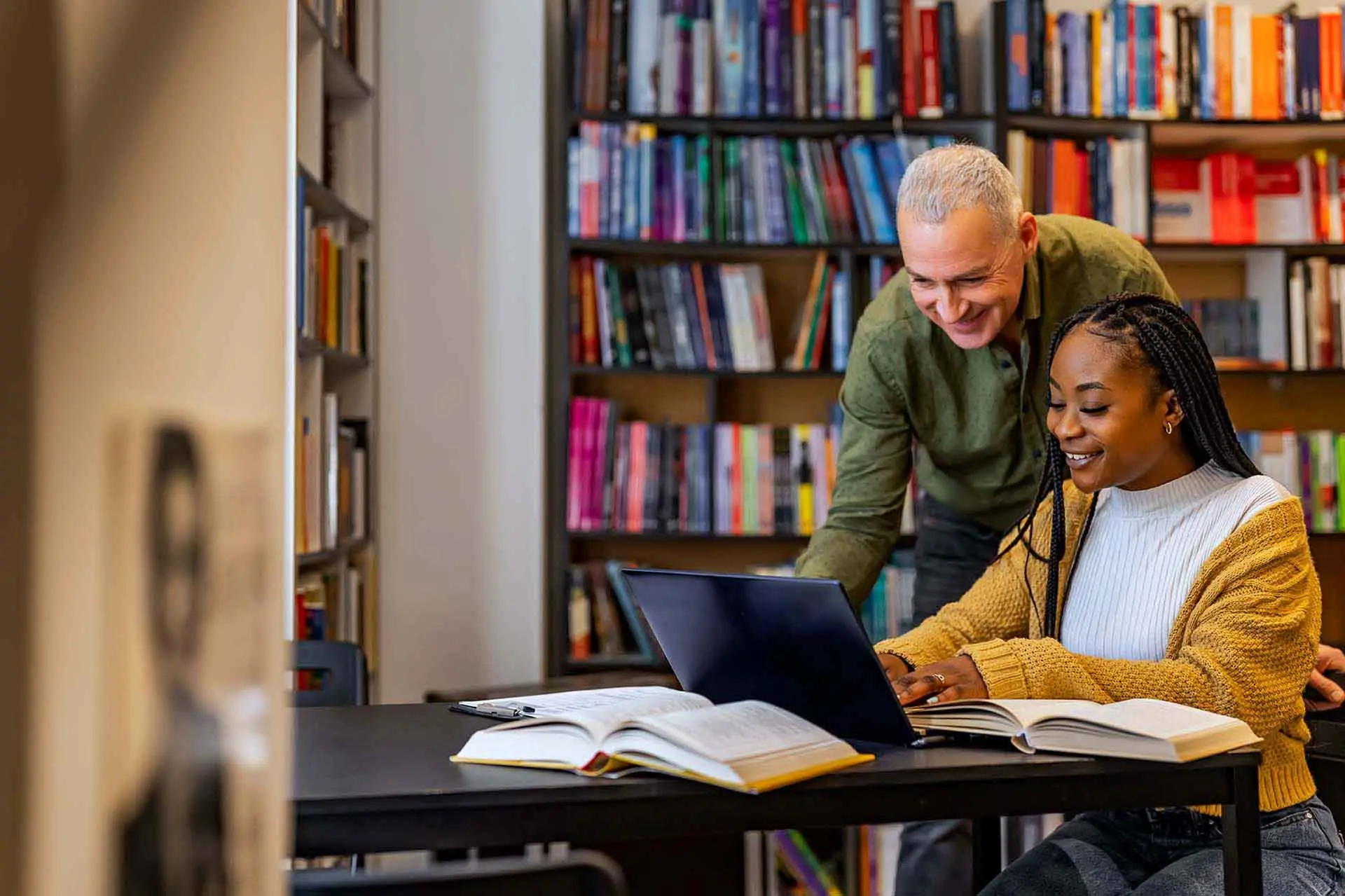 Two people smiling and looking at a laptop with a bookcase in the background